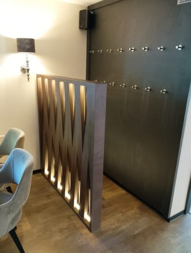 Holzwand mit Lichtakzenten trennt den Raum, daneben eine schwarze Türe mit Haken.