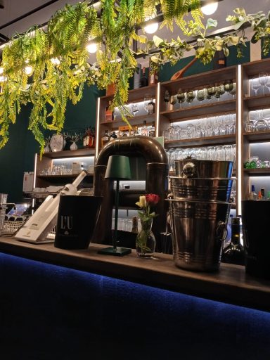 Bar mit Pflanzen, Gläsern und einer Blumenvasen auf der Arbeitsfläche.