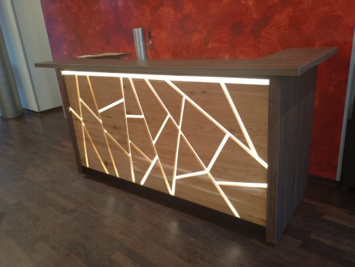 Moderne Empfangstheke aus Holz mit geometrischem Design und integrierter Beleuchtung.