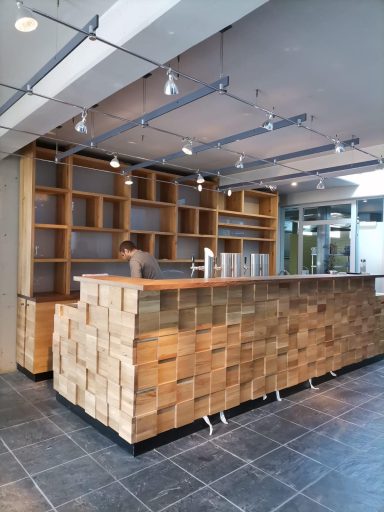 Moderne Empfangstheke aus Holz mit Regalen im Hintergrund und hellen Lichtquellen.