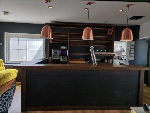 Moderne Bar mit Holztheke und Kupferlampen, minimalistischem Design und leeren Regalen.