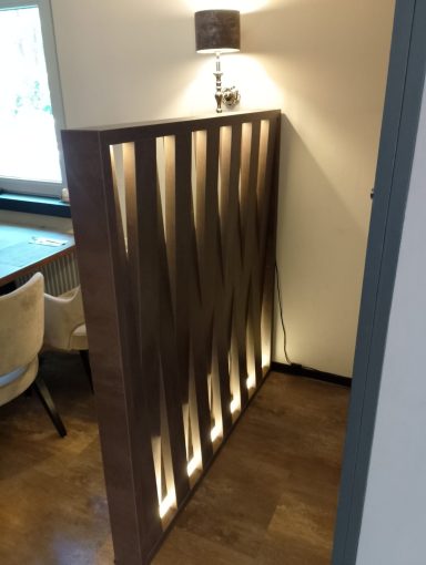 Holzwand mit Wellenmuster und hinterleuchteten Elementen, steht in einem modernen Raum.