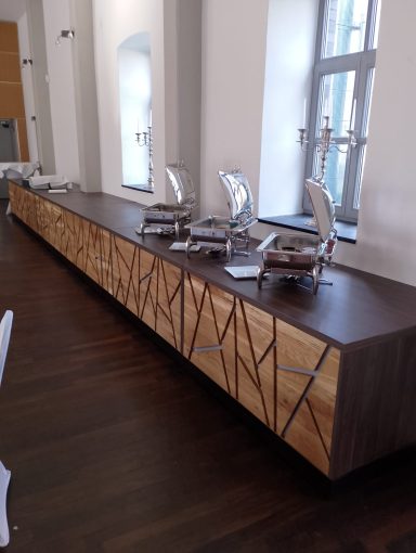 Moderne Holzkommode mit geometrischem Design und weißen Stühlen davor.