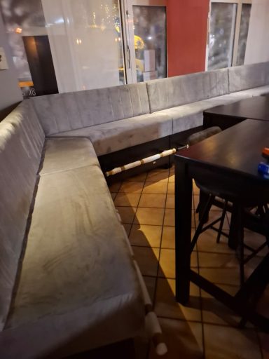 U-förmige Sitzecke mit grauen Polstern in einem Restaurant. Holztisch im Vordergrund.