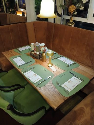 Holztisch mit grünem Besteck und Getränken, gemütlicher Sitzbereich.