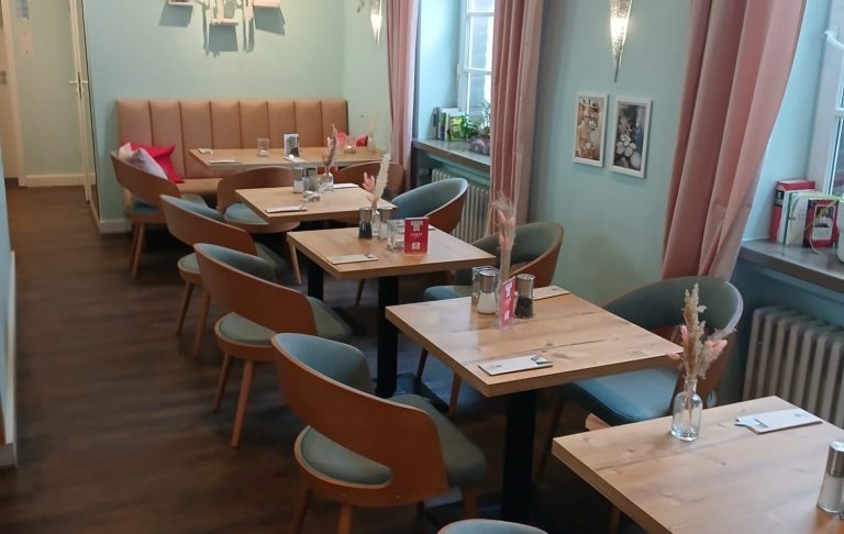 Heller Restaurantbereich mit Holztischen, Stühlen und gemütlicher Atmosphäre.