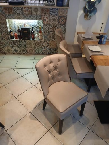 Beige gepolsterter Stuhl vor einem Tisch in einem gefliesten Restaurant.