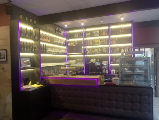 Moderne Bar mit beleuchtetem Regal, Theke und ausgelegtem Verkaufsbereich.