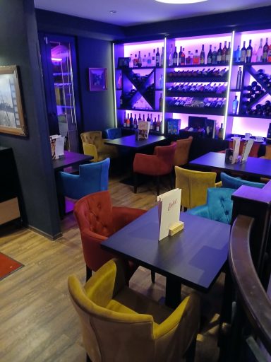 Gemütliche Restaurant-Atmosphäre mit bunten Stühlen und beleuchtetem Regal im Hintergrund.