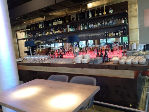 Moderne Bar mit beleuchtetem Tresen, Regalen voller Getränke und eleganten Sitzplätzen.