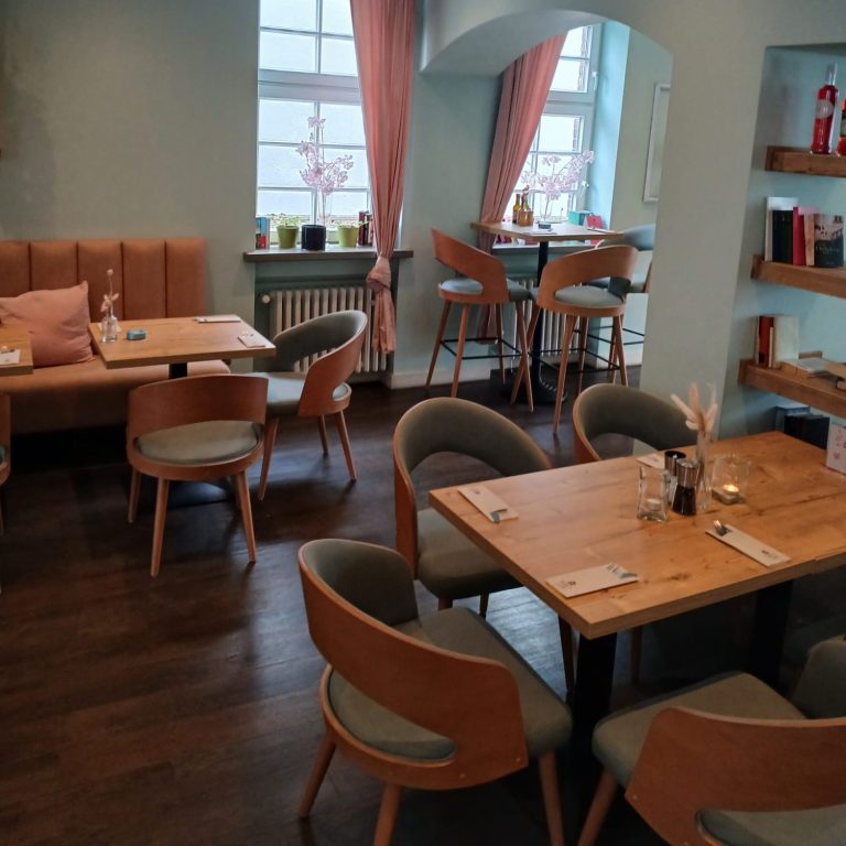 Helles Restaurant mit Holzstühlen, Tischen und einer gemütlichen Atmosphäre.