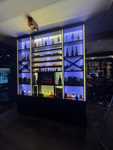 Regal mit beleuchteten Flaschen in verschiedenen Farben hinter einer Bar.