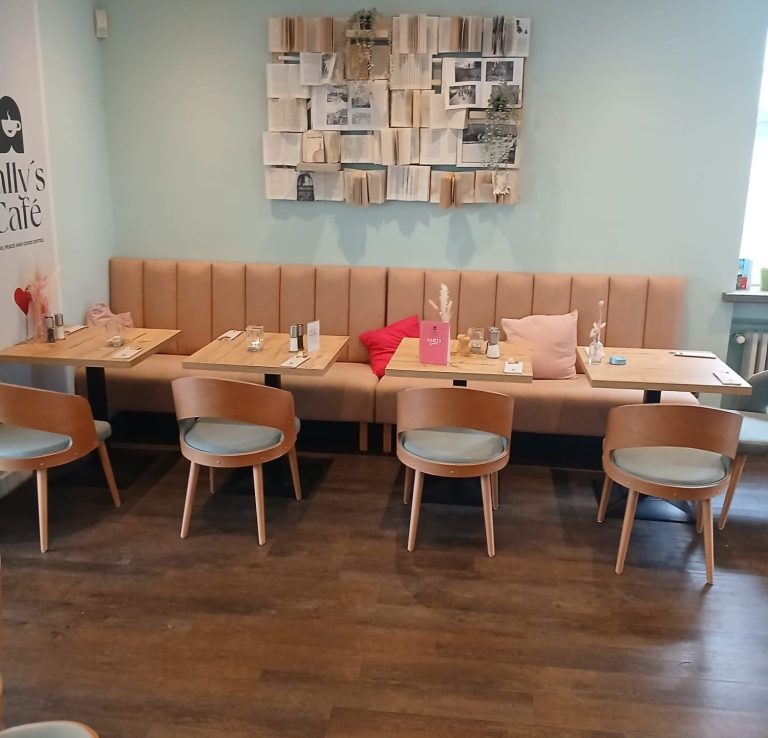 Helle Bistro-Einrichtung mit Holzbank, Tischen und Stühlen in Pastellfarben.