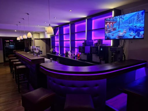 Moderne Bar mit lila Beleuchtung und einem Fernseher im Hintergrund.