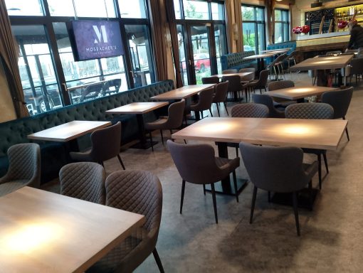 Innenansicht eines Restaurants mit Tischen und Stühlen, hell erleuchtet und modern eingerichtet.